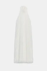 Vestido largo color crudo de cuello halter, sin mangas y con textura de flecos en toda la prenda. Cuenta con espalda descubierta, cierre de botones y lazada a contraste.