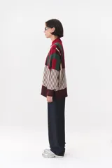Buzo oversize de tejido de punto con diseño de bloques y rayas verticales en colores rojo, verde, bordó y crema. Presenta cuello alto tejido y terminaciones en rib en puños y ruedo.