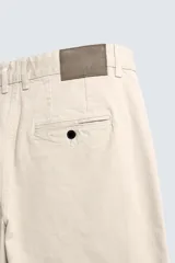 Pantalón chino de algodón color beige claro, corte recto, con cierre frontal de cremallera y botón, bolsillos delanteros y bolsillos traseros de doble vivo con botón.