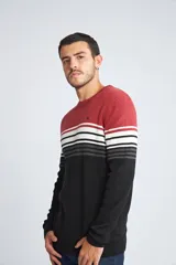 Sweater de punto con diseño de bloques de color, presentando una sección superior roja, una franja central con rayas horizontales en blanco, negro y gris, y una sección inferior negra. Posee cuello redondo, mangas largas y logo bordado en el pecho.