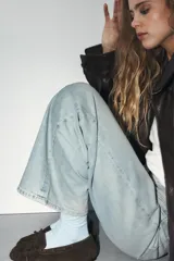 Mocasín de serraje color marrón oscuro, con detalle de fruncido y lazo en la parte delantera, y pasadores decorativos en los laterales.