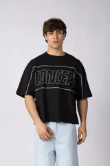Remera negra de corte boxy y mangas cortas, con diseño gráfico en el pecho que incluye la palabra "CONCEPT" delineada en blanco y líneas decorativas alrededor de los hombros y mangas.