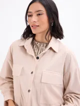 Campera de pana color beige, con cuello camisero, cierre frontal con botones, bolsillos frontales tipo parche y elástico en la cintura.