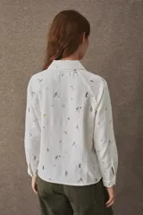 Remera estilo polo de manga larga, confeccionada en una mezcla de algodón y lino. Presenta un cierre frontal parcial, cuello camisero y aberturas laterales en el frente. El diseño incluye un estampado integral con motivos deportivos y un detalle bordado en el pecho.