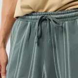 Bermuda de felpa color verde oscuro con diseño de rayas verticales blancas. Cuenta con cintura elástica y cordón ajustable.