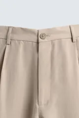 Pantalón de corte relajado confeccionado en tejido con mezcla de lyocell. Presenta cintura con trabillas, cierre frontal con cremallera y botón, pliegues en el delantero, bolsillos laterales y bolsillos traseros de vivo.