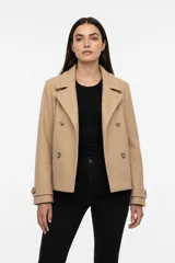 Tapado corto de paño color beige, con diseño de doble botonadura, solapas anchas y mangas largas con detalle de trabilla en los puños.