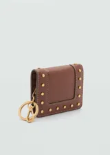 Billetera pequeña de cuero sintético color marrón, con diseño de tachuelas metálicas doradas en el frente y llavero incorporado. Cuenta con cierre de solapa con botón a presión y múltiples ranuras para tarjetas.