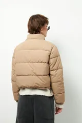 Campera puffer corta color beige de nylon, con cuello alto, cierre frontal y bolsillos laterales con cierre.