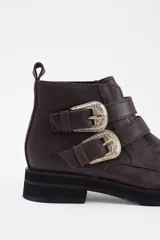 Botín de cuero vacuno color marrón, con punta fina y detalle de tachas metálicas en la parte superior. Presenta una suela de plataforma plana de color negro.