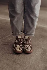 Zapatillas de cuero con estampado que simula pelo de vaca o manchas marrones y blancas. Tienen detalles en cuero marrón liso, cordones marrones y suela de goma color caramelo.