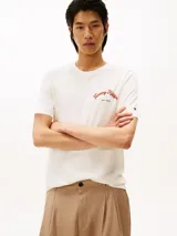 Remera de cuello redondo y manga corta, confeccionada en algodón regenerativo. Presenta un diseño minimalista en color blanco con el logo de la marca bordado en el pecho en tonos cálidos.