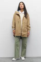 Piloto verde militar de manga larga con capucha y forro de color amarillo. Cuenta con dos bolsillos laterales con solapa, cordones ajustables, elástico en los puños, cierre y botones metálicos.