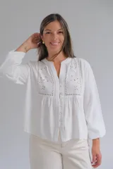 Blusa blanca de manga larga con cuello mao y cierre frontal con botones. Presenta detalles de bordado inglés y calados en la parte superior delantera.