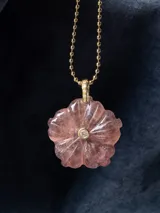 Colgante con dije de piedra natural tallada en forma de flor, con una pequeña circonia incrustada en el centro y engarce de metal dorado, suspendido de una cadena de eslabones tipo bolita.