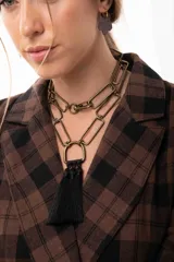 Collar de cadena con eslabones rectangulares en tono bronce, con diseño versátil que permite usarlo largo o doble. Presenta un dije central en forma de herradura con un aplique de borlas de hilo negro.