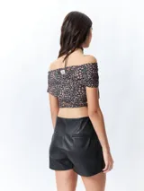 Top negro con estampado floral, escote off-shoulder, corte cruzado y mangas cortas.