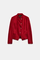 Blazer de terciopelo color rojo, con cuello subido, manga larga y cierre frontal cruzado con botones dorados. Presenta bolsillos delanteros con solapa.