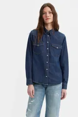 Camisa de denim azul oscuro, de corte recto, con cuello clásico, cierre frontal con botones a presión, mangas largas con puños abotonados, dos bolsillos frontales con solapa y costuras decorativas en los hombros.