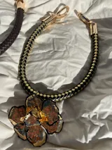 Collar con cordón trenzado de cuero sintético negro y dije redondo plateado con centro de piedra blanca con pintitas negras.