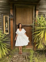 Vestido midi blanco 100% lino, de corte amplio y silueta en capas, con escote en V y mangas cortas adornadas con detalles de costura.