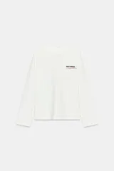 Camiseta de manga larga color blanco, corte regular fit, con cuello redondo y bajo recto. Presenta un pequeño texto estampado en color rojo en el pecho.