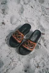 Sandalias tipo chinelas de cuero color suela, con plataforma baja y diseño de capellada con calados geométricos inspirados en motivos pampeanos.