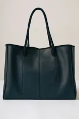 Bolso tipo tote de diseño minimalista, confeccionado en cuero con textura granulada. Presenta una estructura rectangular con costuras verticales decorativas en el frente y doble asa superior para llevar al hombro.