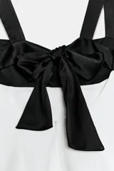 Top de escote cuadrado y tirantes anchos, con diseño bicolor en negro en la parte superior y blanco en el cuerpo, corte ligeramente acampanado y espalda descubierta con lazada.