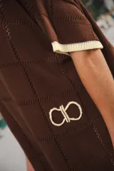 Vestido corto de tejido calado color marrón, con patrón cuadrado y logo bordado a mano en el frente. Presenta terminaciones a contratono en escote redondo y mangas cortas.