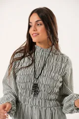 Vestido largo a rayas verticales en tonos verde y blanco, con cuello alto fruncido, mangas largas abullonadas y falda amplia. Presenta un diseño de nido de abeja con hilo elástico hasta la cintura.