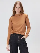 Polera de manga larga confeccionada en tela rib color tostado, con cuello alto y hombreras. Presenta costuras a la vista con pespuntes en hilo de color contrastante en las terminaciones.