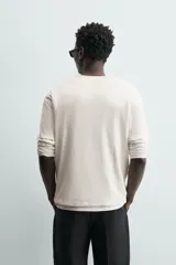 Camiseta de algodón color beige claro, de corte relajado (relaxed fit) con cuello redondo y manga corta. Presenta una textura sutil en el tejido.