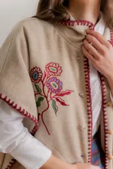 Poncho de paño color beige con flores bordadas en el frente y detalles de costura artesanal en los bordes en color bordó. Cuenta con bolsillos laterales y cierre frontal con botones de madera.