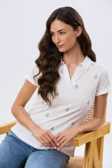 Remera polo de algodón color beige con mangas cortas, escote en V y cuello camisero. Presenta delicados mini bordados florales distribuidos en toda la prenda.
