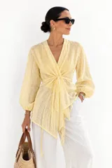 Camisa cruzada de gasa color amarillo claro con diseño de rayas sutiles, escote en V pronunciado, mangas largas abullonadas y lazo ajustable para atar en el frente.