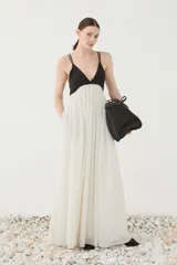 Vestido largo bicolor con escote en V y tirantes finos dobles. Presenta la parte superior ajustada en color negro y una falda amplia y fluida de corte evasé en color blanco marfil, con bolsillos laterales ocultos.