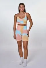 Conjunto deportivo compuesto por un top de escote redondo y un short de tiro alto, ambos con diseño tie-dye en tonos pastel salmón, amarillo y celeste. El top presenta el logo de la marca estampado en el frente.
