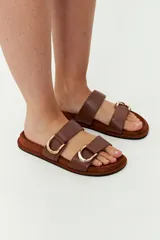 Sandalias marrones con dos tiras anchas de cuero sintético y hebillas metálicas doradas.