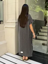 Vestido largo de tejido de punto con diseño de rayas verticales en blanco y negro. Presenta escote en V, mangas cortas y tajos laterales en el ruedo para mayor movimiento.