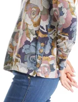 Buzo de hilado fino con cuello redondo y mangas largas. Presenta un estampado floral en tonos grises, azules y ocres, con detalle de botones decorativos en el lateral inferior.