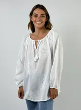 Blusa blanca de algodón con escote con lazo y mangas largas abullonadas. Presenta bordados calados con motivos florales.