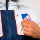 Campera rompevientos Umbro del Club Nacional de Football, con diseño bicolor en blanco y azul marino. Presenta capucha, cierre frontal completo, logo de Umbro y escudo del club en el pecho.