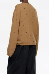 Sweater de punto en color gris oscuro, con corte boxy y escote en caja. Presenta mangas largas rectas y está decorado con pequeños remaches plateados distribuidos por toda la prenda. Confeccionado en una mezcla de lana y alpaca que aporta calidez.