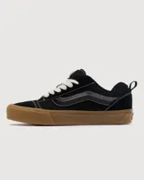 Championes Vans modelo Knu Skool, de estética inspirada en los años 90 con silueta voluminosa. Confeccionados en gamuza negra, presentan lengüeta y cuello acolchados, Sidestripe en diseño 3D y suela de goma color caramelo con patrón waffle.