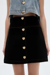 Minifalda de jean blanca de corte recto, con botonera frontal con botones metálicos dorados y costuras pespunteadas a contratono.