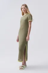 Vestido largo verde de tejido de punto calado, con escote redondo y mangas cortas. Tiene tajos laterales y ribetes en color amarillo.