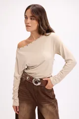 Remera de manga larga color beige con diseño de hombro caído y detalle de tachas metálicas a lo largo del escote.