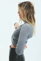 Polera de tejido de punto acanalado, color gris, con cuello alto y mangas largas. Presenta un ajuste al cuerpo y largo hasta la segunda cadera.