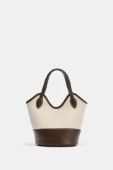 Bolso tipo bucket de diseño estructurado, confeccionado en combinación de canvas color crudo y cuero sintético marrón. Presenta doble asa de mano, pespuntes a contraste y base reforzada.